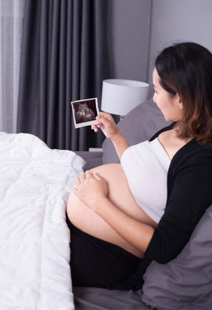 pregnant woman with ultrasound image of baby sitting on bed in b - Valokuva, kuva
