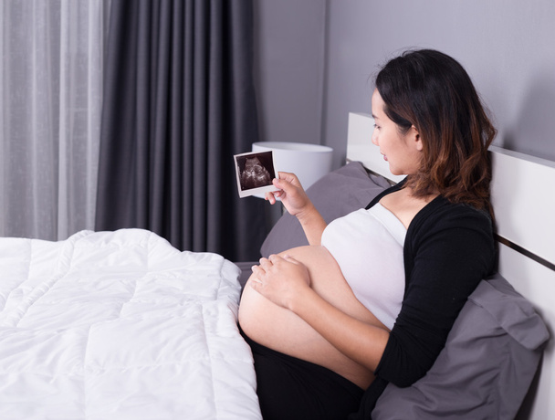 pregnant woman with ultrasound image of baby sitting on bed in b - Foto, imagen