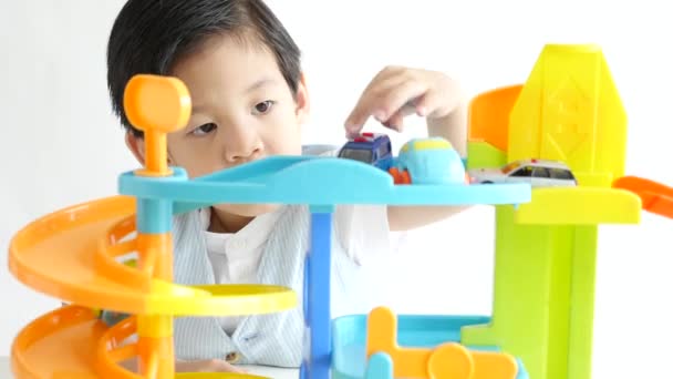 Lindo niño asiático jugando coches de juguete sobre fondo blanco
 - Metraje, vídeo