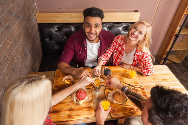 Grupo de pessoas comendo fast food hambúrgueres batata sentada na mesa de madeira no café vista do ângulo superior
 - Foto, Imagem
