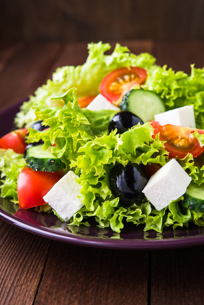 griechischer Salat (Salat, Tomaten, Feta-Käse, Gurken, schwarze Oliven) auf dunklem Holzgrund in Nahaufnahme. - Foto, Bild