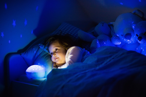 Menina na cama com lâmpada noturna
 - Foto, Imagem