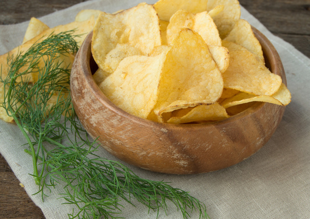 Knusprige Kartoffelchips mit Dill in einer Holzschüssel auf Leinenserviette - Foto, Bild