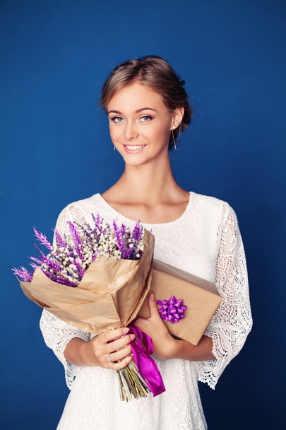 Молодая улыбающаяся женщина с цветами и подарочной коробкой
 - Фото, изображение