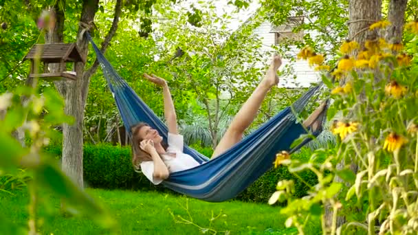The girl in a hammock. He is talking on the phone and smiling. HD - Footage, Video