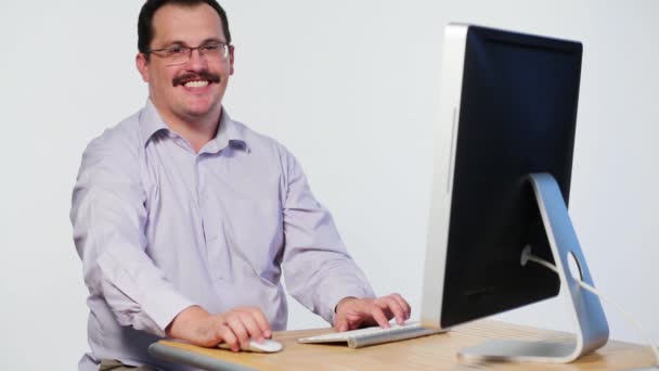 Satisfied man sits at desk with computer, smiles and types - Felvétel, videó