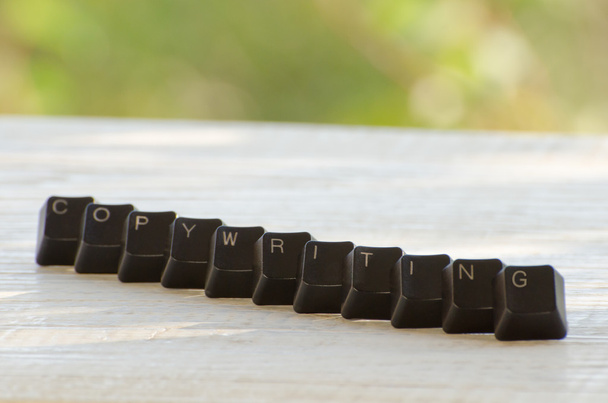 Из черных клавиш клавиатуры составлено слово Копирайтинг на белом столе под открытым небом
 - Фото, изображение