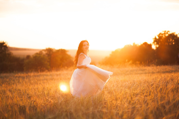 Happy beautiful young bride outside on a summer meadow at the sunset - Zdjęcie, obraz