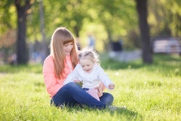 Happy mother and daughter in the park. Beauty nature scene with family outdoor lifestyle. Happy family resting together on the green grass, having fun outdoor. Happiness and harmony in family life. - Фото, зображення