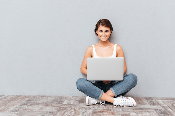 Smiling woman sitting on the floor with laptop computer - Фото, зображення