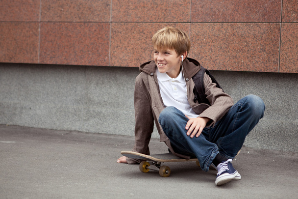 School teen sits on skateboard near school - Photo, Image