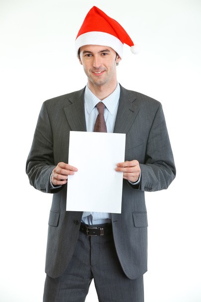 Smiling businessman in Santa's hat showing blank paper - Foto, Bild