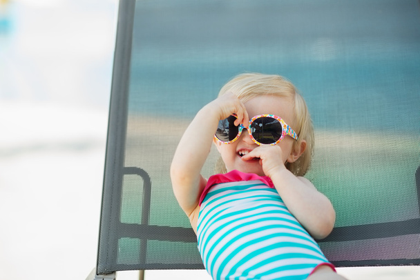 Portrait of baby in swimsuit and sunglasses laying on sunbed - Foto, immagini