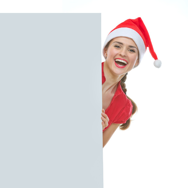 Smiling woman in Christmas hat looking out from blank billboard - Foto, Imagen