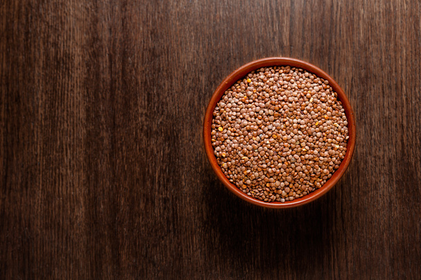 Rustic ceramic bowl of uncooked red lentils isolated on dark wood from above - Photo, Image
