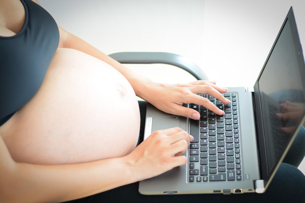 беременная женщина печатает на клавиатуре ноутбука
  - Фото, изображение