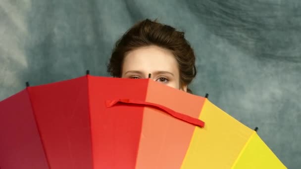 Smiling young brunette woman with multi-coloured umbrella - Materiał filmowy, wideo