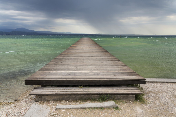 Muelle de madera con olas en Lago di Garda, Sirmione, Italia
 - Foto, Imagen