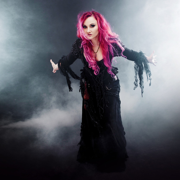 Halloween-Hexe zaubert. attraktive Frau mit roten Haaren im Hexenkostüm, ausgestreckte Arme, starker Wind - Foto, Bild
