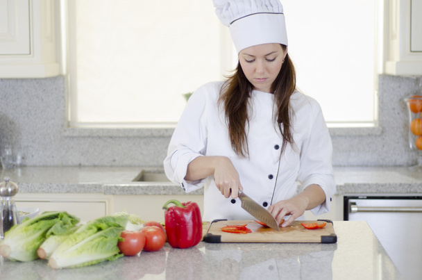 Beautiful brunette working in the kitchen cutting vegetables - Foto, afbeelding
