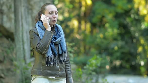 νεαρή κοπέλα μιλάει στο τηλέφωνο στο πάρκο - Πλάνα, βίντεο