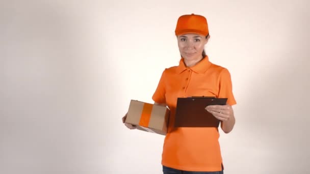Female courier in orange uniform holding a cardboard box. 4K studio shot, isolated - Πλάνα, βίντεο