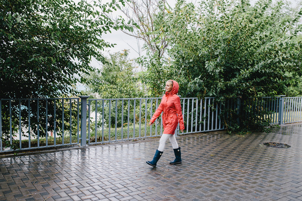 junge Frau in roter Jacke und blauen Gummistiefeln im Regen im Park - Foto, Bild