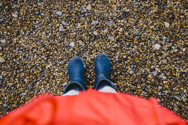 cropped image of a female legs in dark blue rubber boots standing on wet gravel - 写真・画像