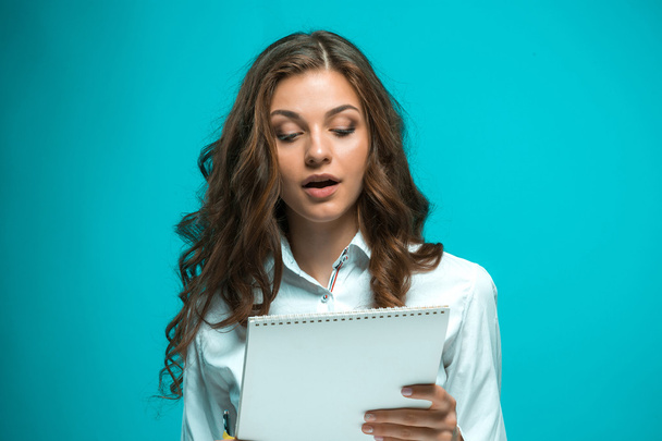 Surprised young business woman with pen and tablet for notes on blue background - Zdjęcie, obraz