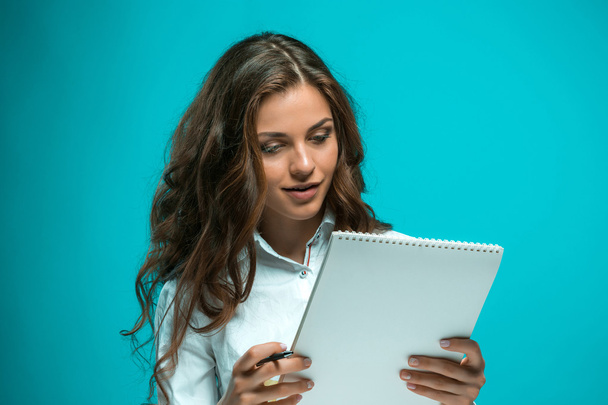 The smiling young business woman with pen and tablet for notes on blue background - 写真・画像