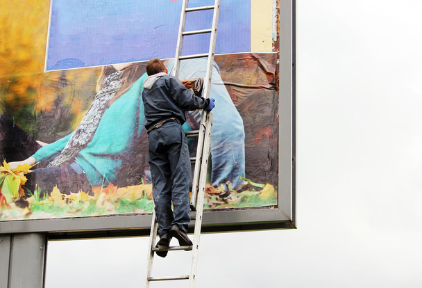 young worker glues a poster with a picture of a autumn girl on a billboard. - Fotó, kép