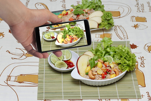 Met behulp van mobiele telefoon te nemen foto een gerecht van gebakken rijst met gemengde groente voor aandeel op sociale netwerk. Selectieve focus. - Foto, afbeelding