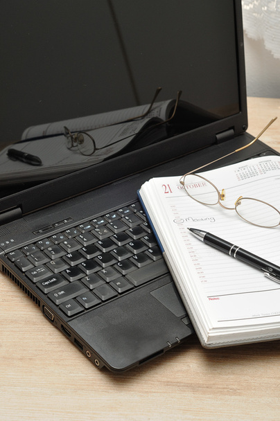 Un portátil con gafas de lectura, un bolígrafo y un diario abierto
 - Foto, Imagen