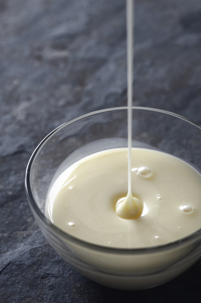 Pouring condensed milk in the glass bowl vertical - Zdjęcie, obraz