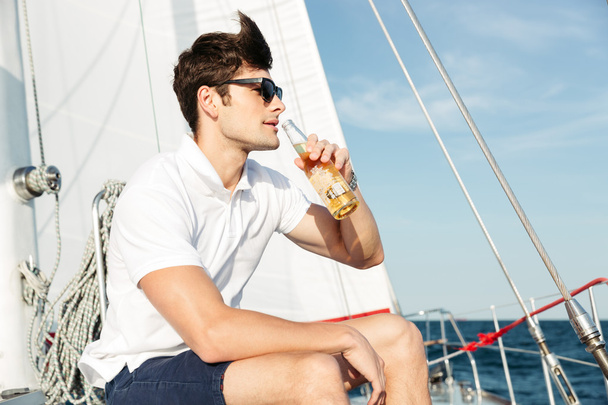Handsome young man drinking beer while resting on the yacht - Фото, зображення