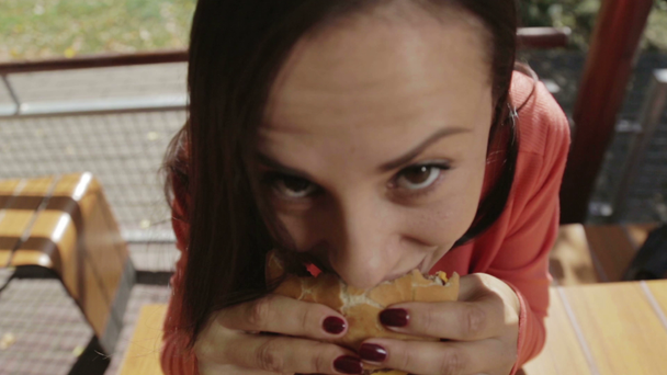 Πορτρέτο του ένα close-up κορίτσι με ένα χάμπουργκερ στο χέρι του. Μια νεαρή όμορφη γυναίκα τρώει χάμπουργκερ σε ένα καφέ. Διατροφή τροφίμων, Fast Food,. - Πλάνα, βίντεο