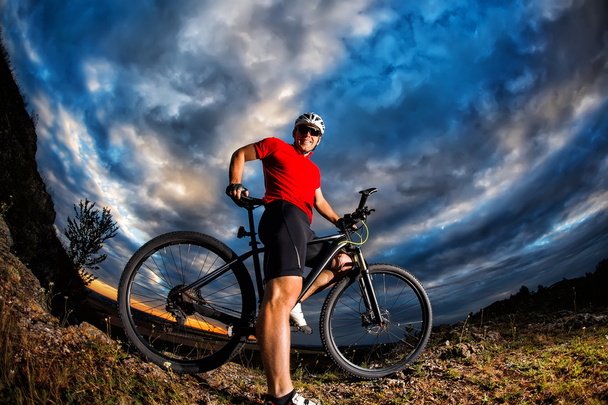 ciclista de pé com mountain bike na trilha ao pôr do sol
 - Foto, Imagem