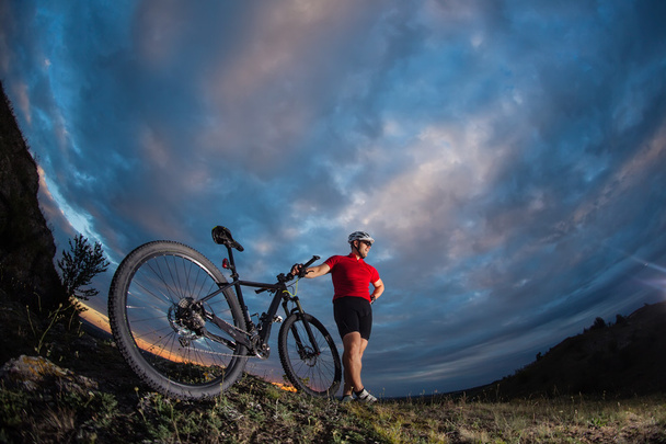 Radfahrer steht bei Sonnenuntergang mit Mountainbike auf Wanderweg - Foto, Bild