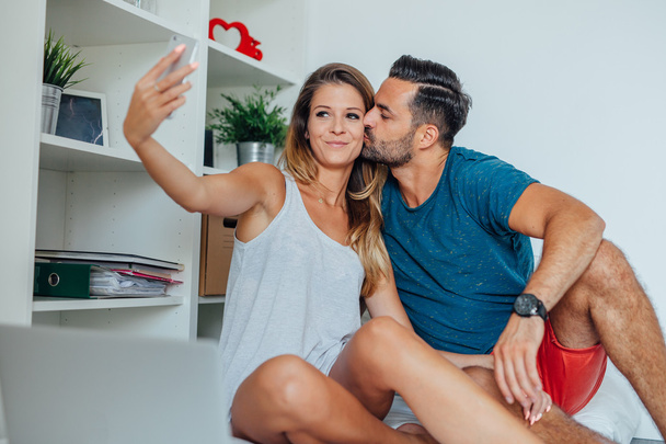 Woman and man are sitting on the bed and taking selfie by smartp - Фото, зображення