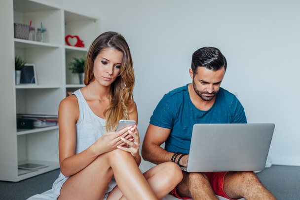 Young couple is sitting on the bed while using pc laptop and mob - Φωτογραφία, εικόνα