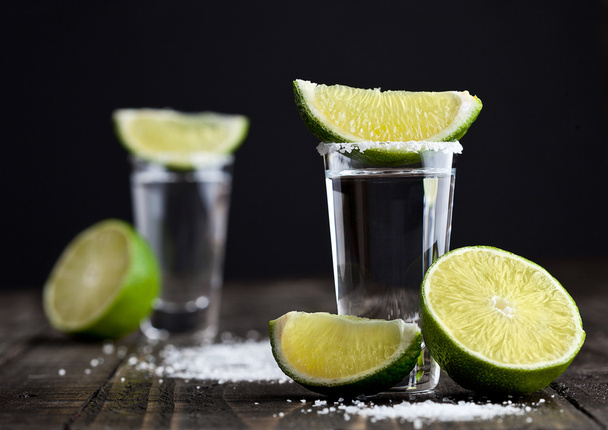 Tequila silver shots with lime slices and salt on wooden board - Фото, изображение