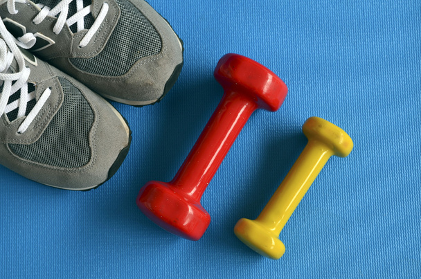 Dumbbells, sneakers and blue yoga mat.Fitness equipment. - Photo, image