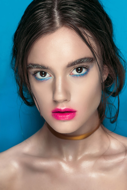 Ομορφιά κορίτσι πορτρέτο με ζωηρό μακιγιάζ. Μόδα γυναίκα πορτρέτο κοντά στο μπλε φόντο. Φωτεινά χρώματα. Μανικιούρ μακιγιάζ. Καπνισμένα μάτια, μεγάλες βλεφαρίδες. Χρώματα ουράνιου τόξου. Αναριχτεί πυροβολισμός - Φωτογραφία, εικόνα