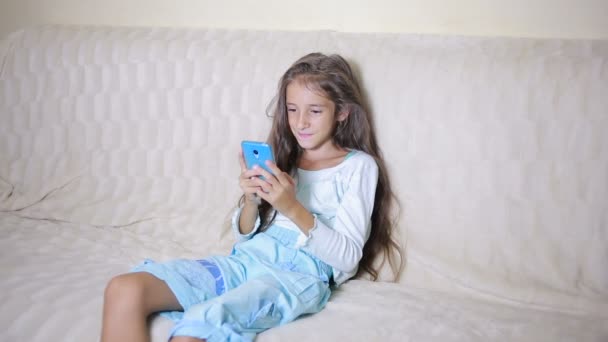 Girl child with a cell phone browses the Internet - Materiał filmowy, wideo