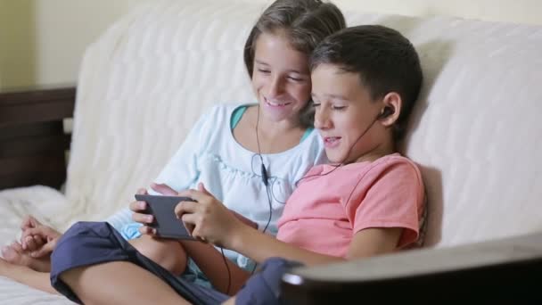 Teenagers using smartphone with earphones. brother and sister with a phone - Imágenes, Vídeo