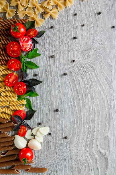 Mixed of two colored pasta near tomatoes, garlic and basil on grey wooden  background. Raw  frame. Copy space. - Photo, Image