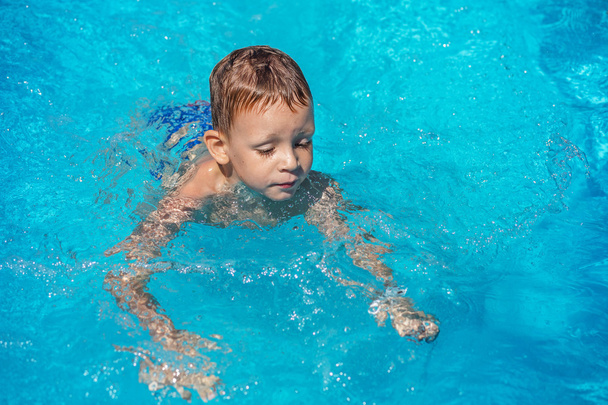 Happy kid playing in blue water of swimming pool. - Photo, Image