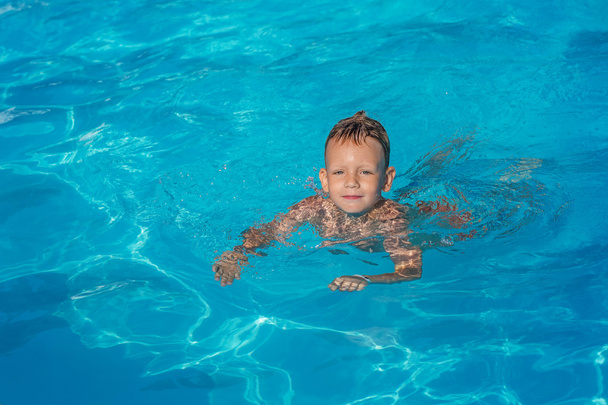 Happy kid playing in blue water of swimming pool. - Photo, Image