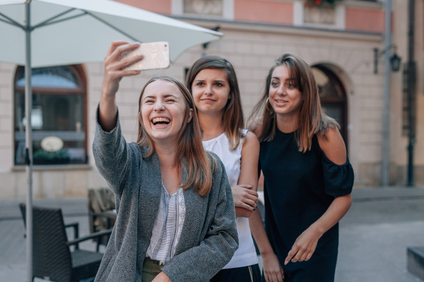 Three girls are taking selfie using mobile phone. City backgroun - Photo, Image