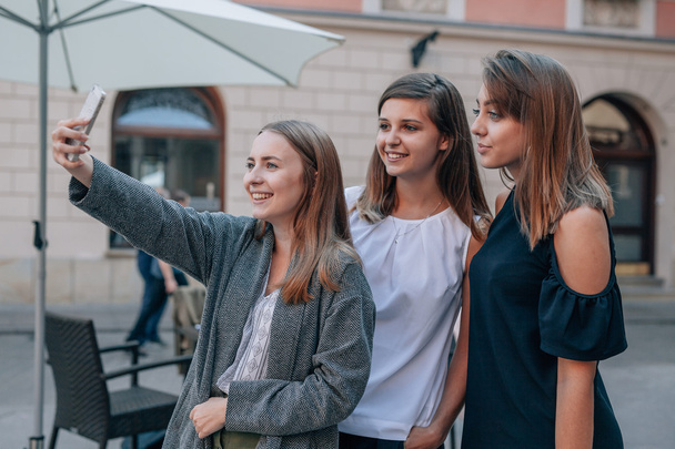 Three girls are taking selfie using mobile phone. City backgroun - Foto, afbeelding